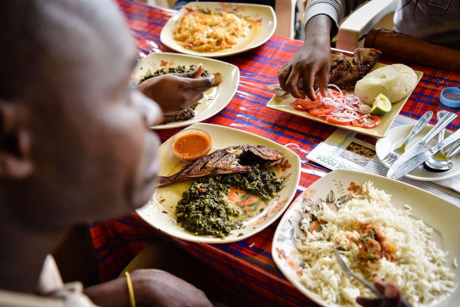 a screenshot taken in Africa of people sitting around a table eating fish